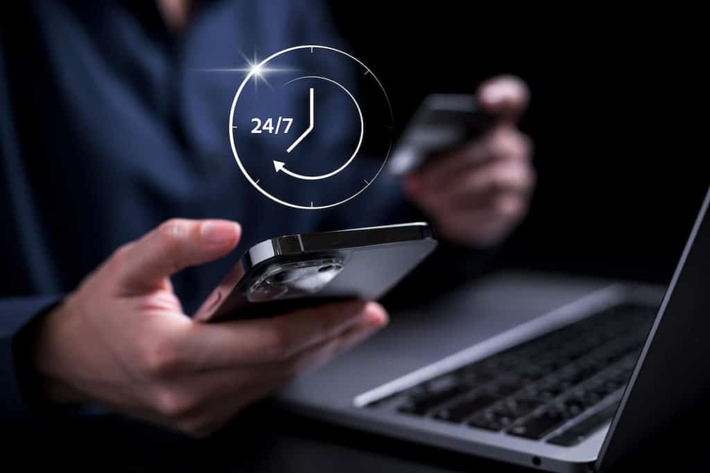 Mensch steht mit Smartphone in der Hand am Laptop