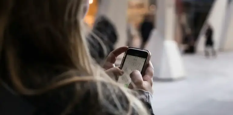 Junge Frau hält Smartphone in der Hand und tippt eine Telefonnummer ein